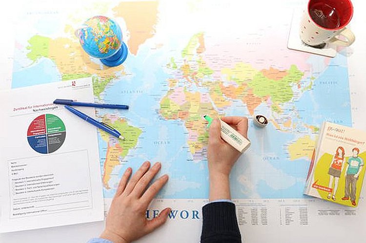Ein Mensch markiert mit einem Stift Orte auf einer großen Weltkarte.