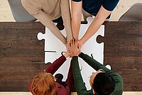 Auf dem Foto sind die Arme und Hände von vier Personen zu sehen. Die Personen stehen im Kreis, ihre Hände treffen sich in der Mitte