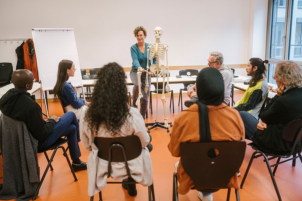 Studierende demonstriert einer Studiengruppe etwas an einem Skelett