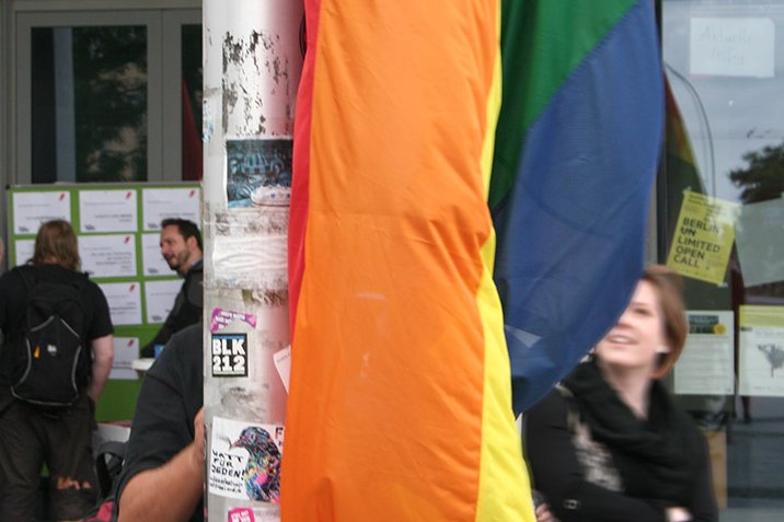 Detailansicht der Regenbogenflagge vor der ASH Berlin, dahinter verschwommen ein lachendes Gesicht