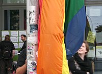 Detailansicht der Regenbogenflagge vor der ASH Berlin, dahinter verschwommen ein lachendes Gesicht