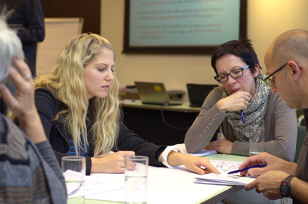 Vier Menschen sitzen in einer Diskussionsrunde am Tisch innerhalb des Master of Arts Studiengangs Klinische Sozialarbeit.