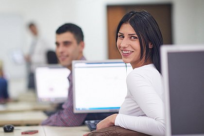 Eine Studentin sitzt lächelnd an einem Rechner, das Gesicht zum Fotografen gewandt.