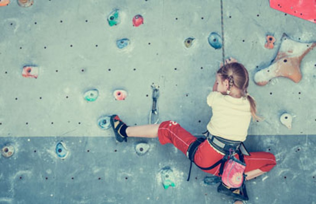 Ein kleines Mädchen klettert an einer Kletterwand.