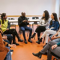 Studierende der ASH Berlin sitzen in einem Seminarraum der Hochschule, in einem Kreis, und diskutieren miteinander.
