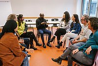 Studierende der ASH Berlin sitzen in einem Seminarraum der Hochschule, in einem Kreis, und diskutieren miteinander.