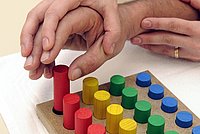 Eine Hand führt ein Kind bei einem Steckspiel