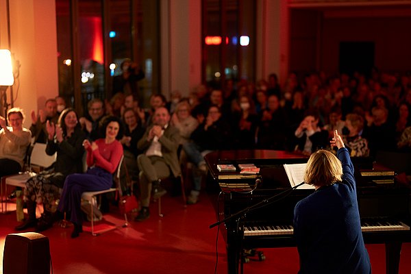 Bernadette La Hengst am Klavier, hinter ihr das Publikum