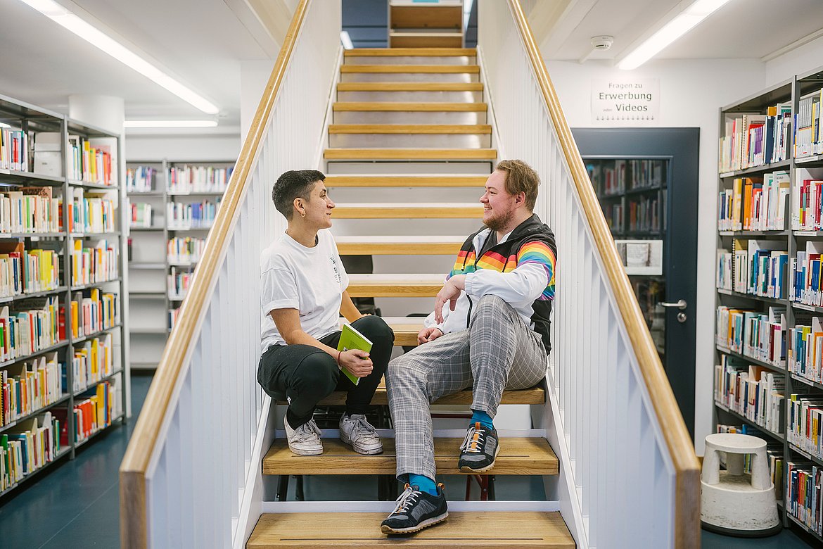 Zwei Studierende sitzen auf der Treppe in der Bibliothek.