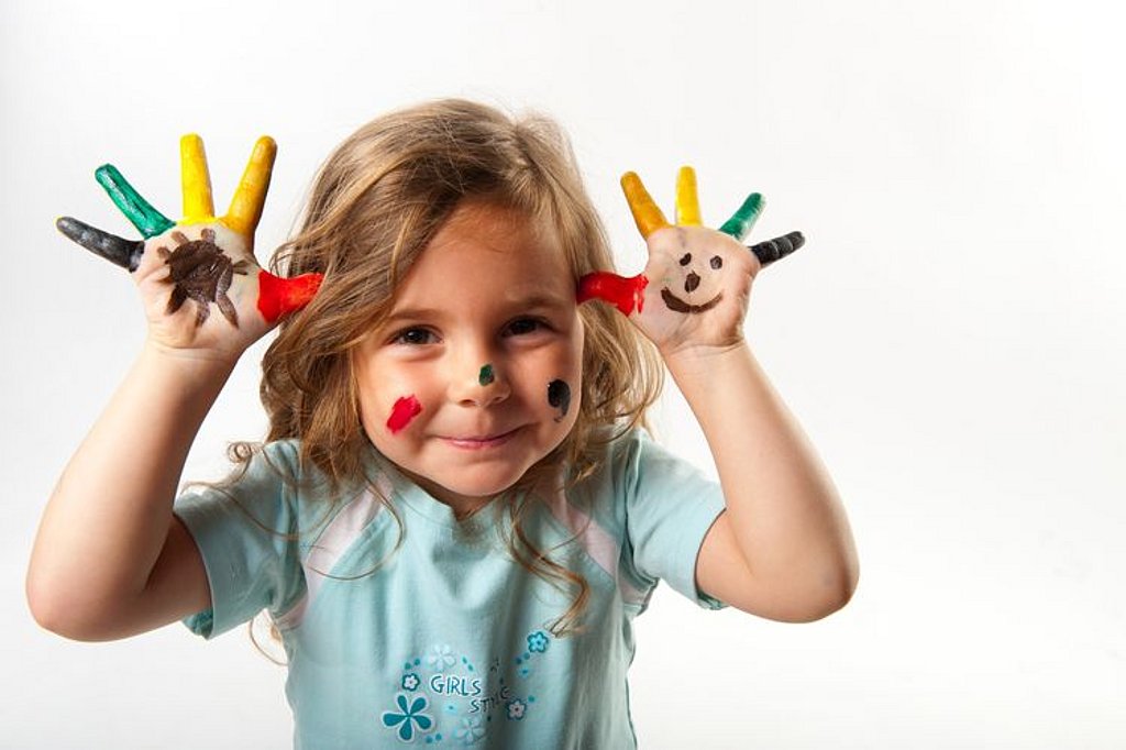 Ein kleines Kind hat bun angemalte Finger und hält sie gespreizt vom Kopf ab