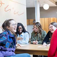 Studierende der ASH Berlin sitzen an einem Tisch, unterhalten sich und lachen dabei 