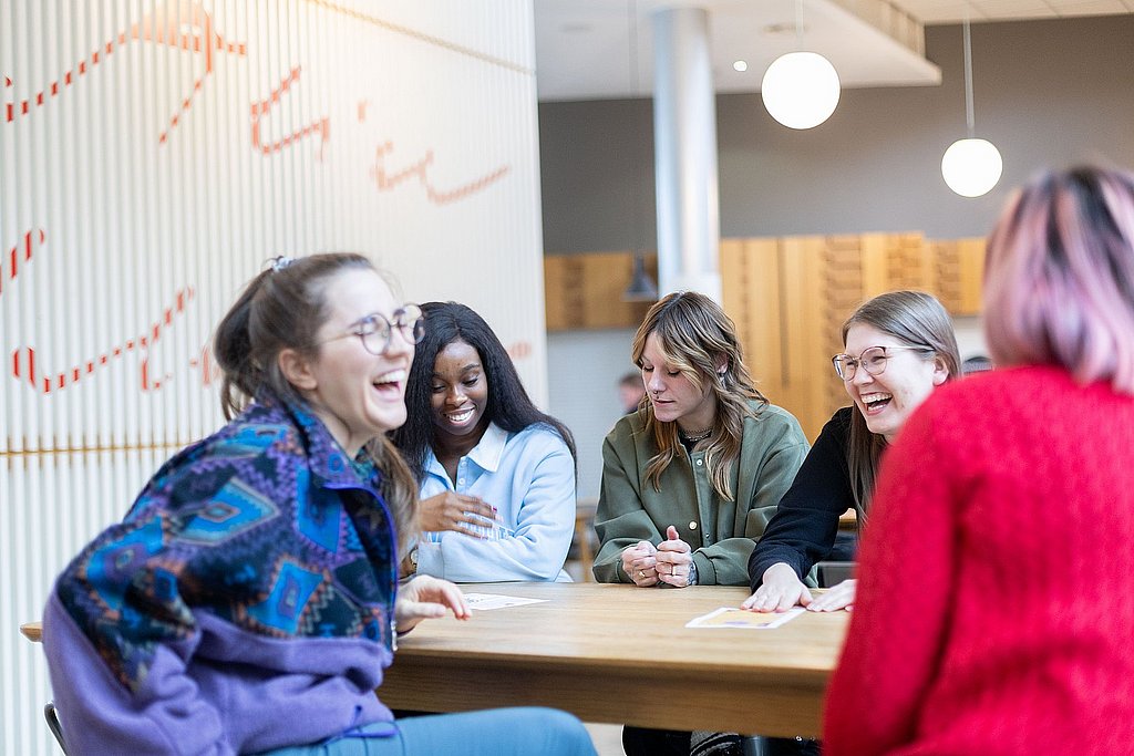 Studierende der ASH Berlin sitzen an einem Tisch, unterhalten sich und lachen dabei 