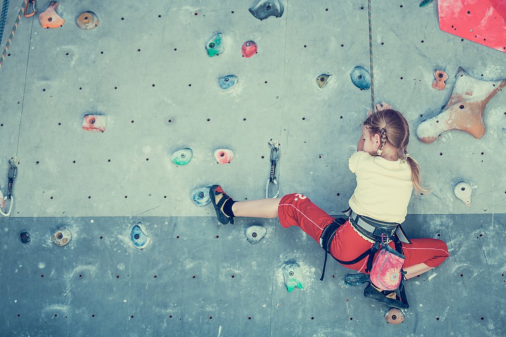 Mädchen klettert an einer Kletterwand hoch
