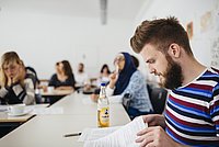 Studierende der ASH Berlin sitzen in einem Seminarraum, hören einem Vortrag zu und blättern durch ihre Seminarunterlagen. 