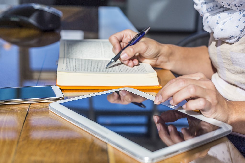 Eine Studentin arbeitet gleichzeitig mit Buch Tablet und Smartphone