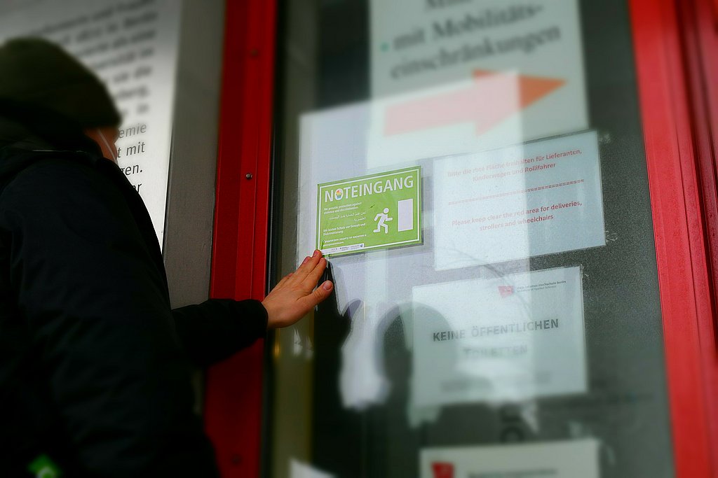 Eine Person bringt am Haupteingang der ASH Berlin den "Noteingang"-Aufkleber an. 
