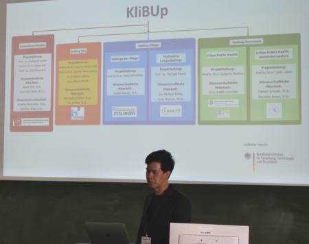 Eine Personhält einen Vortrag mit einer Päsentationsfolie im Hintergrund.