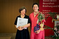 Yevgenia Belorusets und Bettina Völter auf der Bühne des Audimax der ASH Berlin. Belorusets hält die Urkunde in den Händen und Völter trägt einen kleinen Olivenbaum.