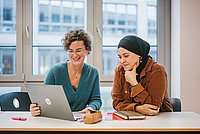 Zwei Frauen sitzen vor einem Laptop.