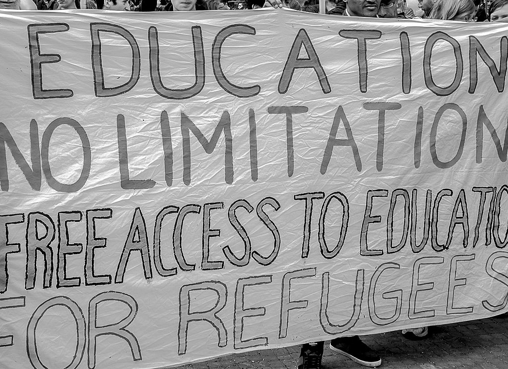 Several people hold a banner during a demonstration. It reads "Education no limitation, free access to education for refugees"