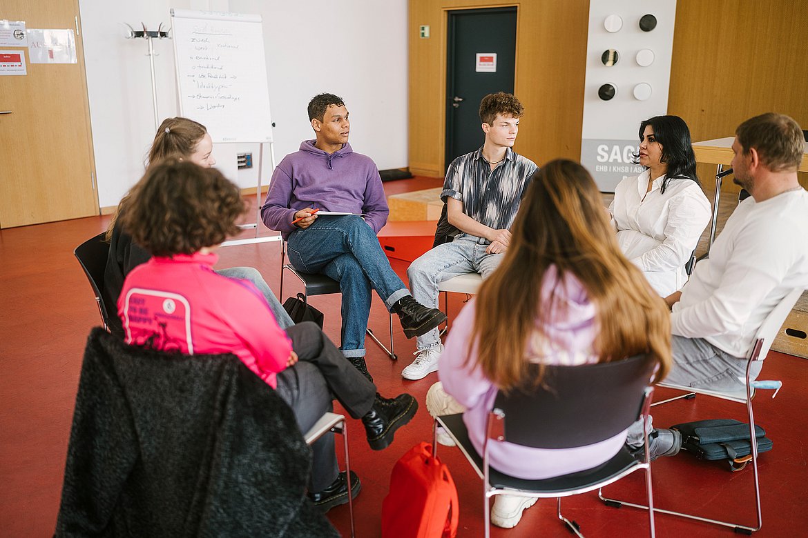 Studierende der ASH Berlin sitzen in einem Stuhlkreis im Audimax der Hochschule und unterhalten sich. 