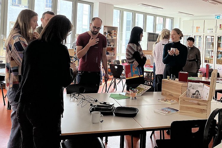 Tagungsteilnehmer_innen stehen in der Hochschullernwerkstatt Kommunikation und Sprache an der ASH Berlin und unterhalten sich