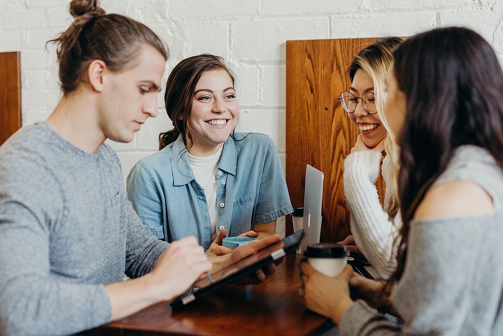 4 Personen sitzen am Tisch und diskutieren fröhlich, Austausch, Mentoring
