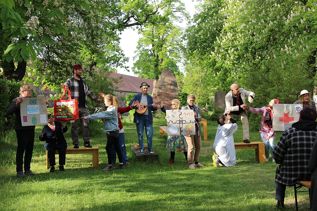 Auf dem Foto sind zahlreiche Menschen zu sehen, die inmitten eines Dorfes Theater spielen. 