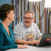 Eine Frau und ein Mann sitzen in ein Gespräch vertieft vor einem Laptop an der ASH Berlin