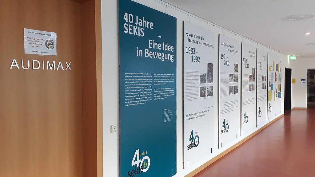 Das Foto zeigt den Flur vor dem Audimax. An den Wänden neben der Tür hängen die Plakate der Ausstellung.