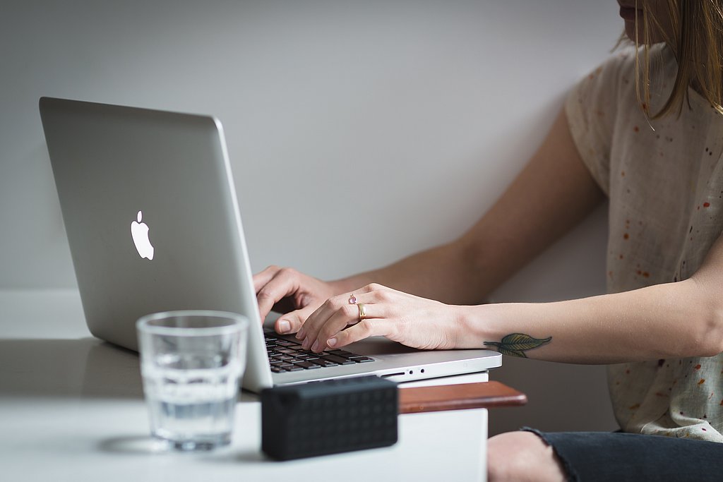 Zeigt eine Frau die vor einem Laptop sitzt und arbeitet