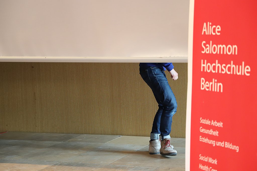 Christoph Szalay beim Tanzen hinte der Projektorleinwand - lediglich die Beine sind zu sehen. Rechts im Bild ein rotes Roll-up der ASH.