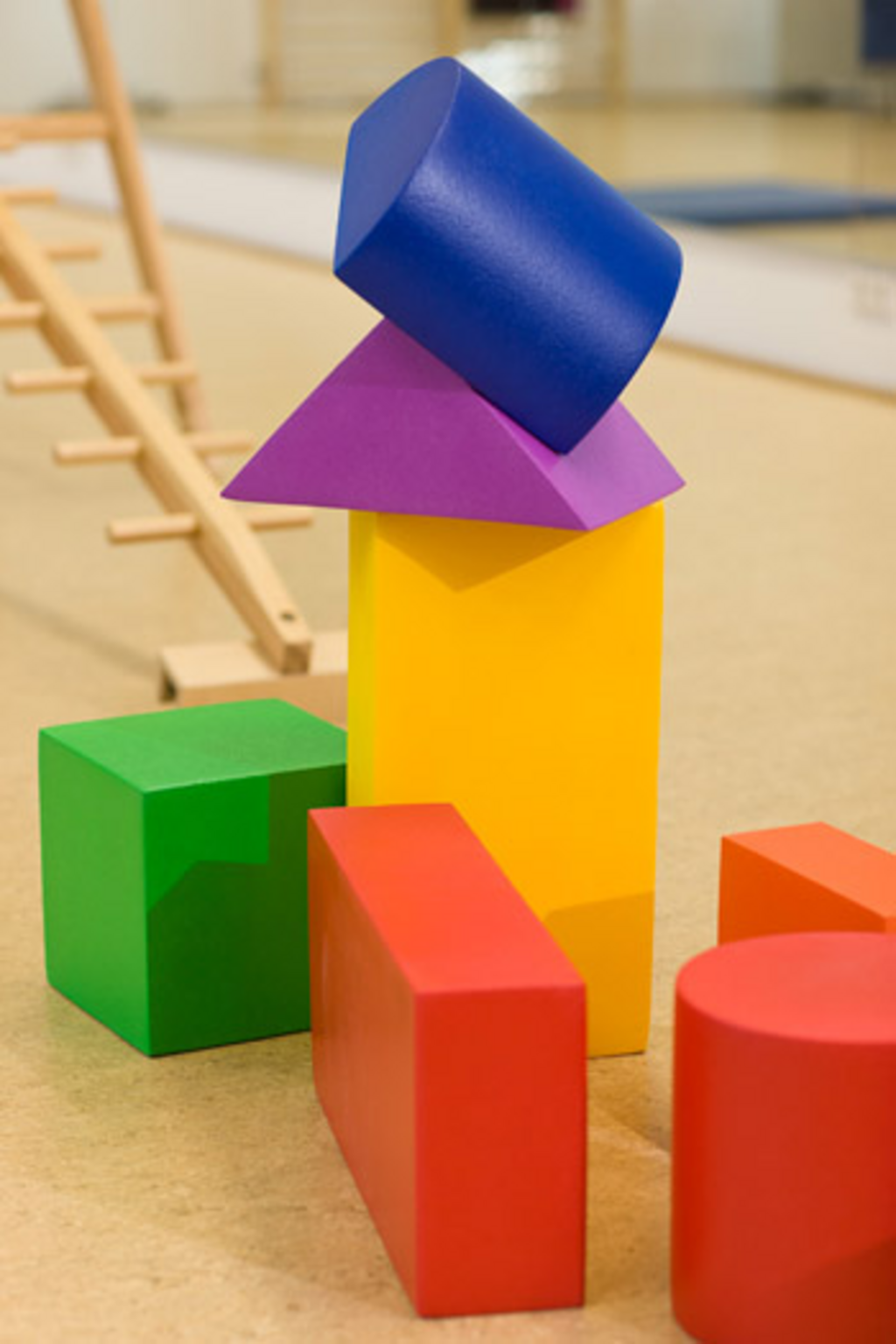 Schaumstoffklötze in verschiedenen Formen bilden zusammen mit einer horizontal aufgestellten Holzleiter eine Parcoursstrecke.