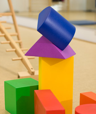 Schaumstoffklötze in verschiedenen Formen bilden zusammen mit einer horizontal aufgestellten Holzleiter eine Parcoursstrecke.