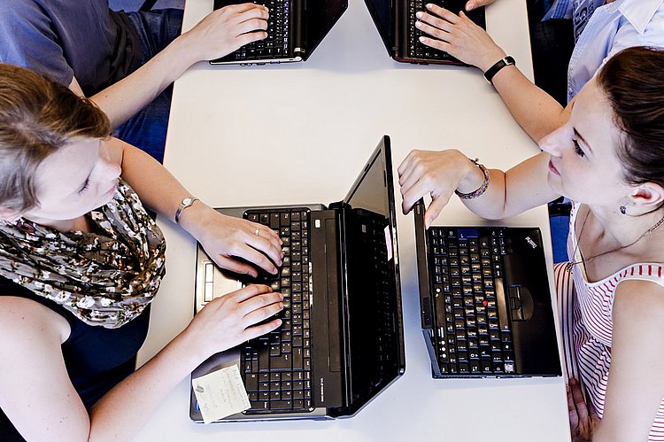 Blick von oben auf zwei Studierende, die sich gegenüber sitzen und jeweils an einem Laptop arbeiten.