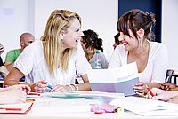 Zwei Studentinnen haben ein Lehrbuch vor sich aufgeschlagen und unterhalten sich angeregt über den Text.