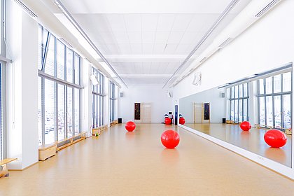 ASH Berlin Bewegungsraum mit roten Bällen Spiegelwand Fensterreihe und Holzboden