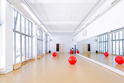 ASH Berlin Bewegungsraum mit roten Bällen Spiegelwand Fensterreihe und Holzboden