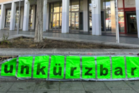 Foto vom Haupteingang der ASH Berlin. Vor der Hochschule sind Plakate zu sehen auf denen das Wort "unkürzbar" steht.