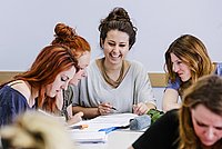 Drei Studentinnen des Master of Arts Studiengangs Biografisches und Kreatives Schreiben sitzen an einem Tisch und machen Notizen.