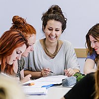 Drei Studentinnen des Master of Arts Studiengangs Biografisches und Kreatives Schreiben sitzen an einem Tisch und machen Notizen.