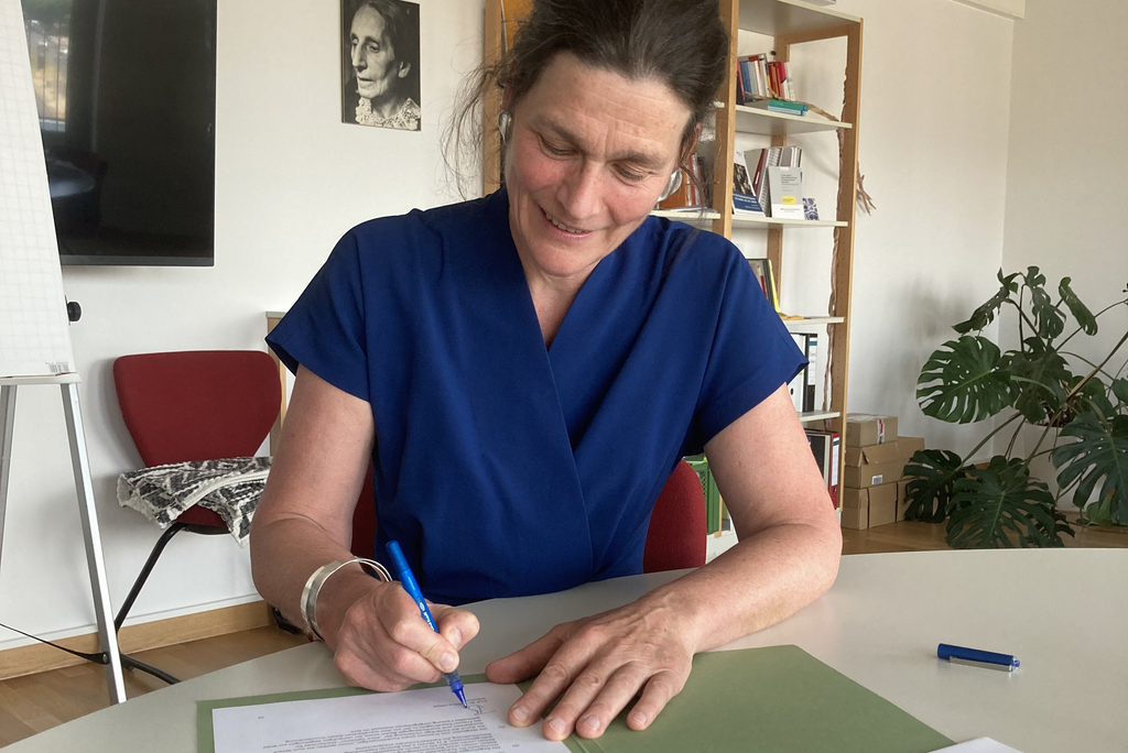 Bettina Völter sitzt an einem Tisch und unterzeichnet die Grundordnung der ASH Berlin