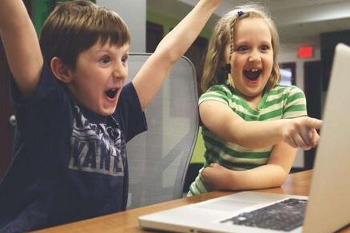zwei Kinder reißen die Hände vor einem Laptop in die Höhe