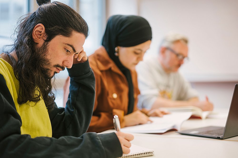 Drei Studierende schreibend im Seminarraum.