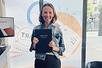 Auf dem Foto ist Jennifer Hübner zu sehen. Sie steht in einem Copyshop und hält ihre frisch gedruckte Dissertation in den Händen. 