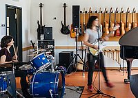 E-Gitarre, Schlagzeug und Flügel- eine Gruppe Studierender musiziert zusammen.