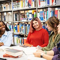 Studierende der ASH Berlin sitzen in der Bibliothek an einem Tisch und unterhalten sich