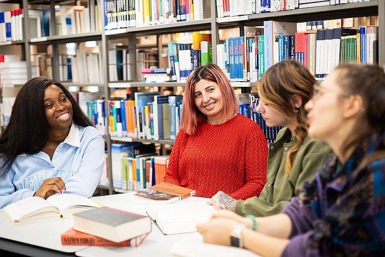 Studierende der ASH Berlin sitzen in der Bibliothek an einem Tisch und unterhalten sich
