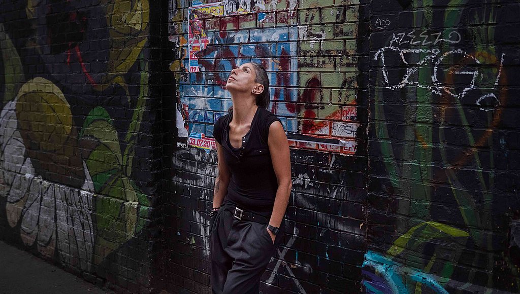 Das Foto zeigt DJ Ipek, die sich an eine Hauswand lehnt und nach oben schaut