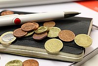 Nahansicht eines Notizbuches, auf dem viel Kleingeld und ein Stift liegt.